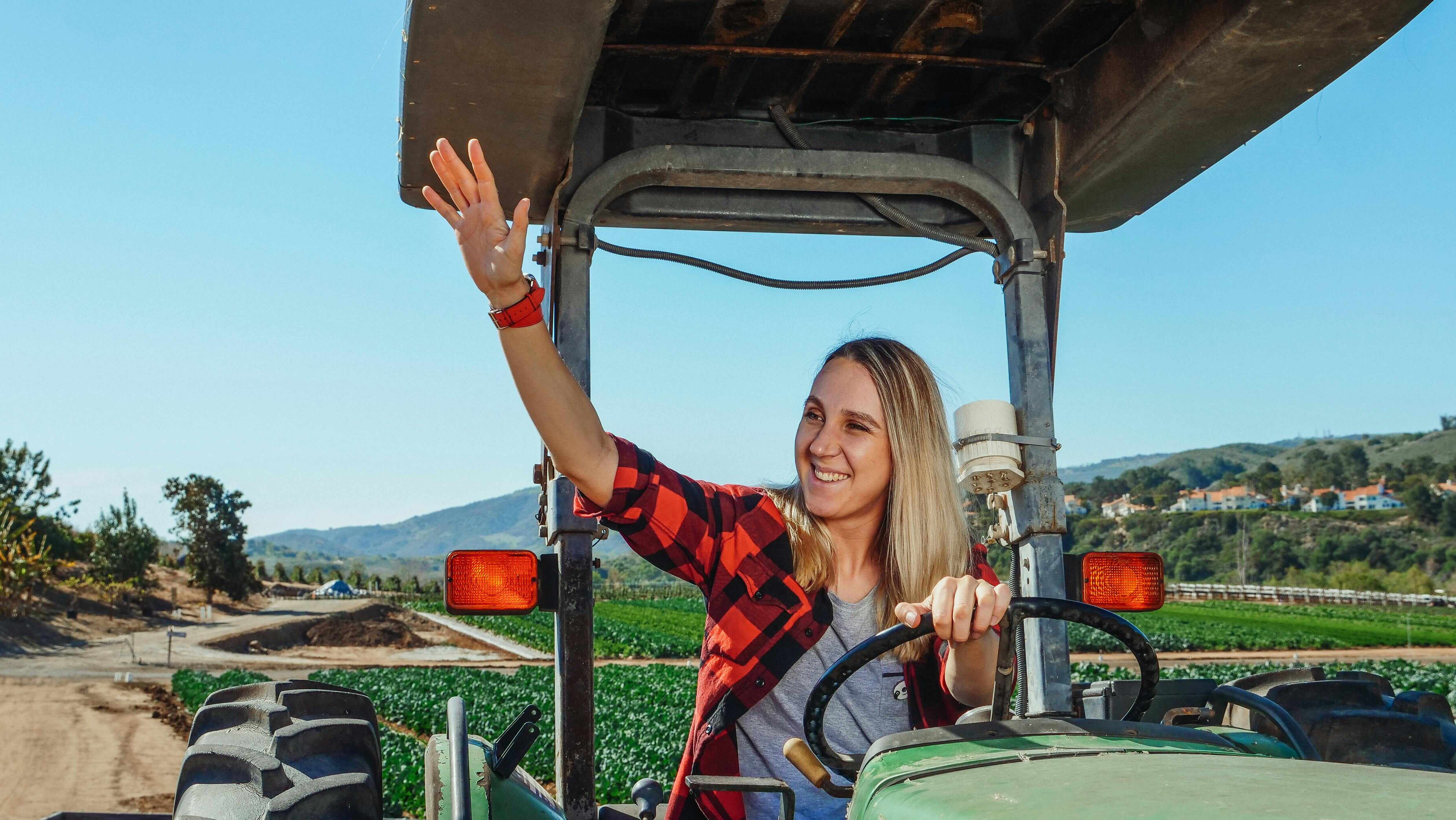 woman waving and driving a tractor in agricultural area